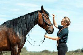 Caucasian woman holding reins of horse with hand in outdoors.